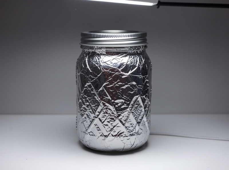 A hydroponic jar neatly wrapped in aluminium foil to block all light from the reservoir under a grow light
