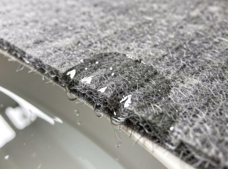 Close-up of a wet grey capillary mat edge draped over a water reservoir tray with water wicking into the felt
